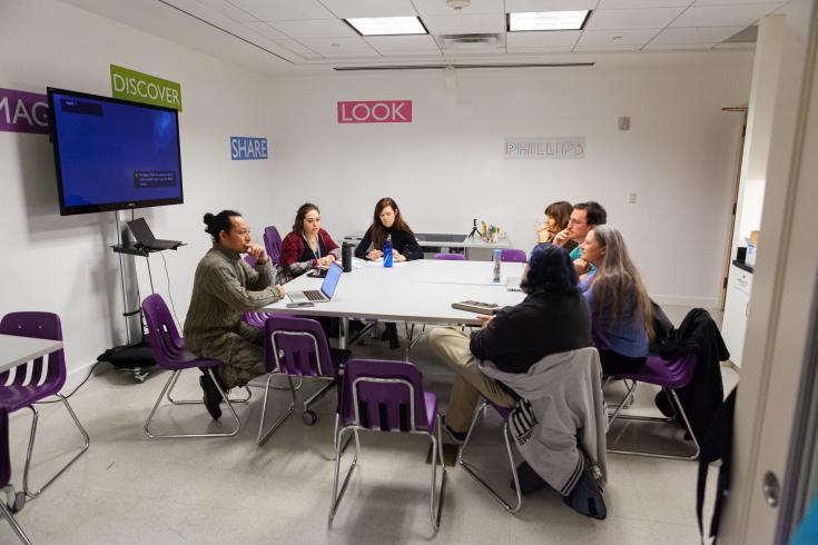 Photograph of group of people sitting around a table in a room with white walls