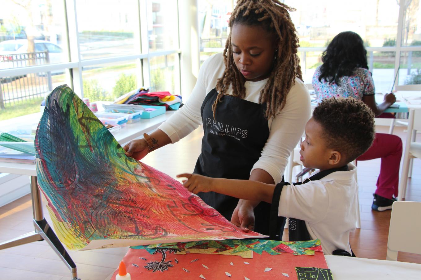 A mother and son creating a painting together in a room with a lot of windows