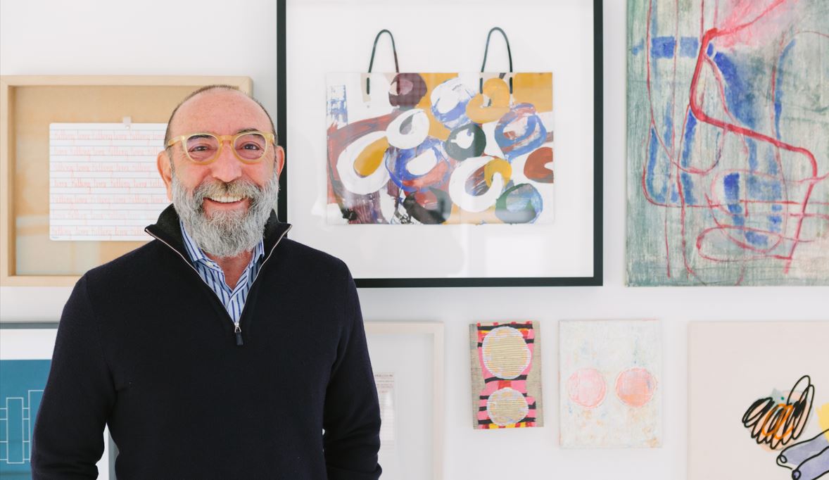 Photograph of Dani Levinas smiling in front of a wall of artwork