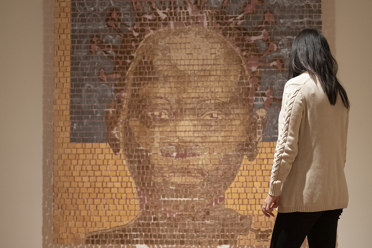 Photograph of a person standing in front of a large artwork of someone's face