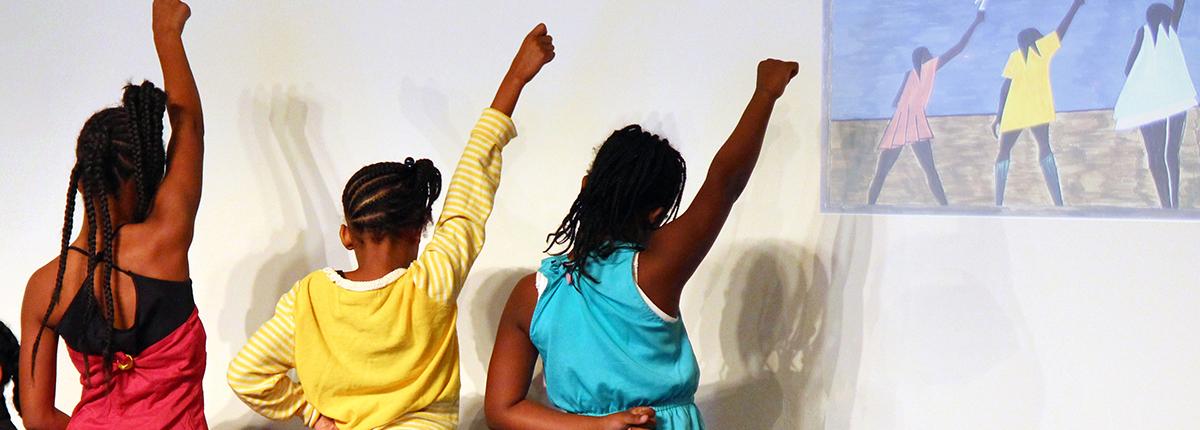 Photograph of three girls mimicking an artwork that is projected on a wall