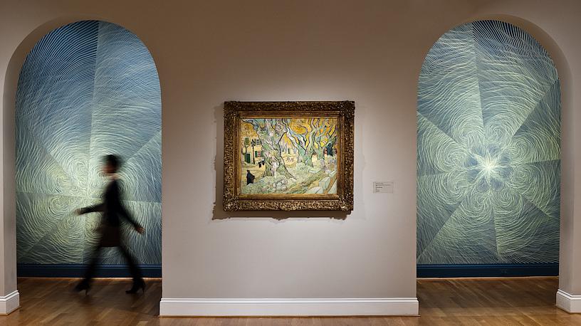 Photo of a figure walking in front of walls with drawings by linn meyers, with a painting by Van Gogh on display 