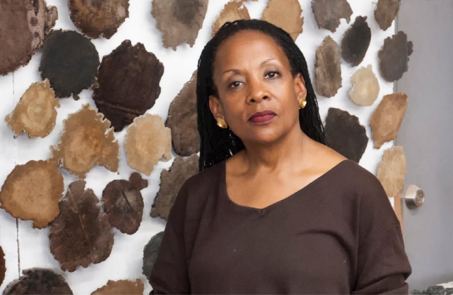 Headshot of a woman standing in front of a lot of brown circular artwork on the wall