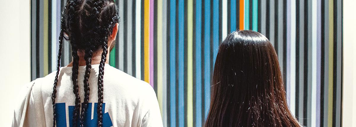 Photograph of two people standing looking at a striped painting