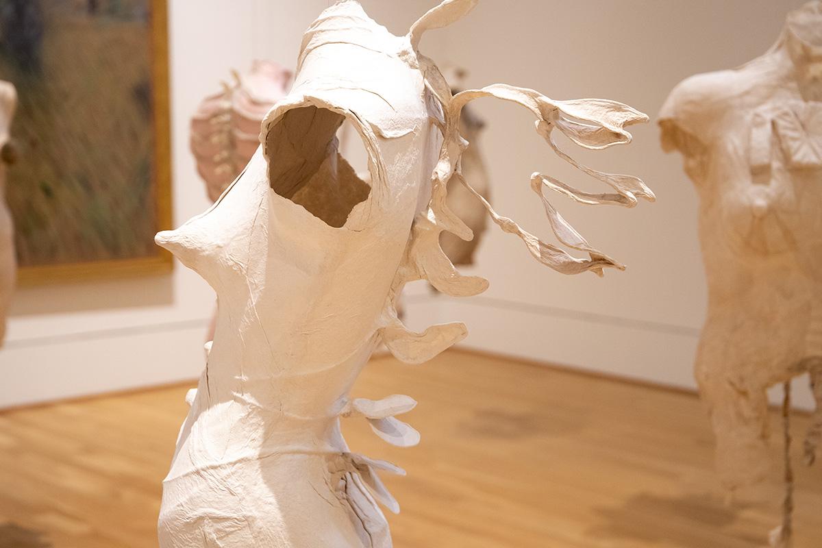 Photograph of paper sculptures of abstract female torsos hanging in gallery