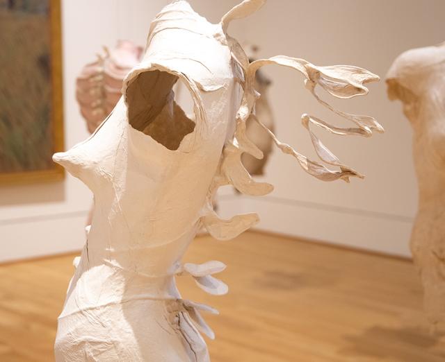 Photograph of paper sculptures of abstract female torsos hanging in gallery