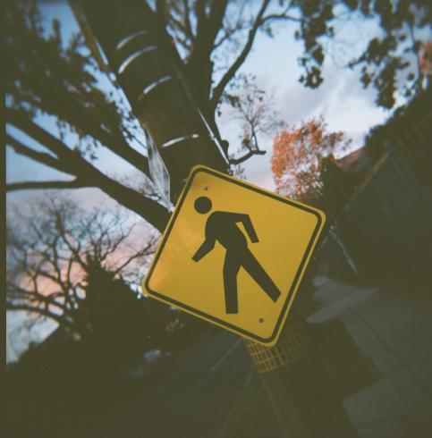 Image of a yellow crosswalk sign against a sunset sky 