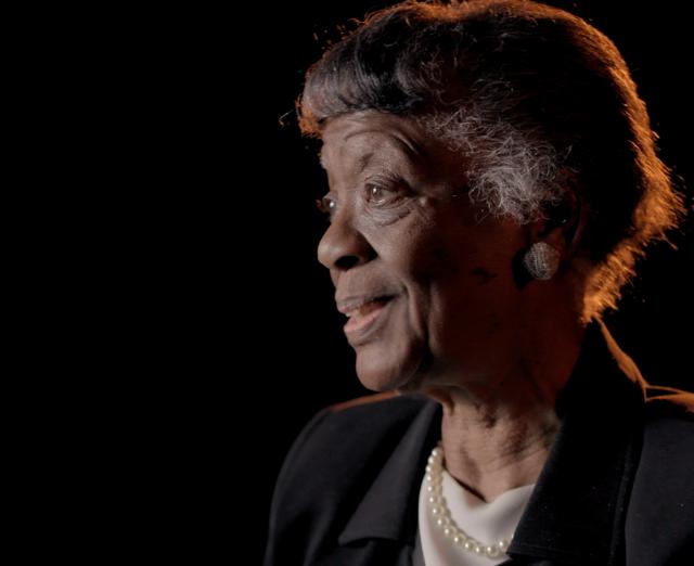 Close-up photo of an older woman against a black background looking off to the left