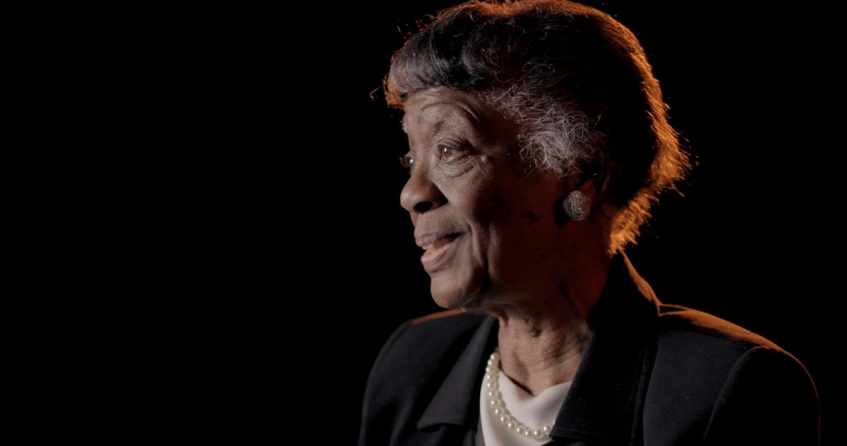 Close-up photo of an older woman against a black background looking off to the left